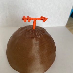 May include: A brown 3D printed dome with an orange arrow on top.