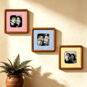 May include: Three square wooden picture frames with rounded corners, each featuring a different coloured gingham fabric border in pink, blue, and yellow. Each frame holds a black and white photograph of a couple making playful facial expressions.