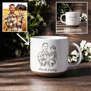 May include: White ceramic mug with a brown base, featuring a black and white sketch of a man holding a child. The mug has the text "Alan & Daddy" at the bottom. A smaller image shows the mug with the word "Daddy" and a heart.