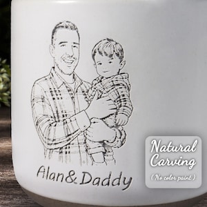 May include: A white ceramic mug with an engraved image of a father and child. The text "Alan & Daddy" is etched below the image. The mug also features the text "Natural Carving (No color paint)".