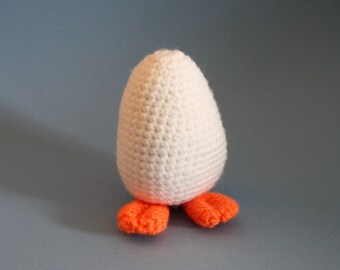 Peut inclure: Un œuf en crochet blanc avec des pieds orange. L'œuf est debout sur un fond bleu.
