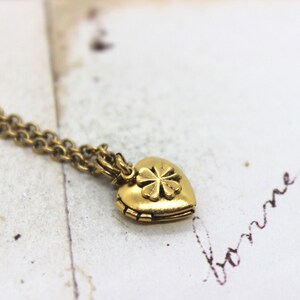 May include: A gold heart-shaped locket necklace with a four-leaf clover design on the front.