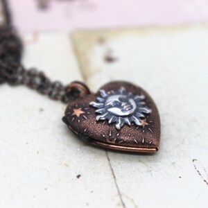 May include: A copper heart-shaped locket necklace with a silver sun and moon design. The locket is decorated with small stars and has a textured finish.