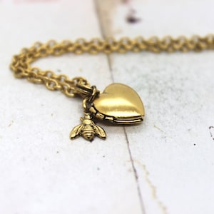 May include: A gold heart-shaped locket necklace with a small bee charm. The locket is open and the chain is visible.