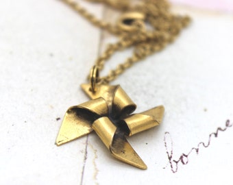 May include: A gold-toned necklace with a charm in the shape of a bow. The bow is made of metal and has a twisted design.