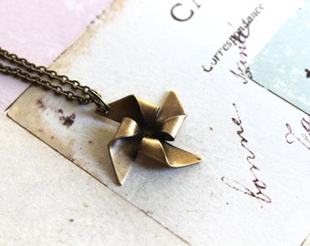 May include: A gold-toned necklace with a delicate, origami-style windmill pendant. The pendant is made of metal and has a slightly textured finish.