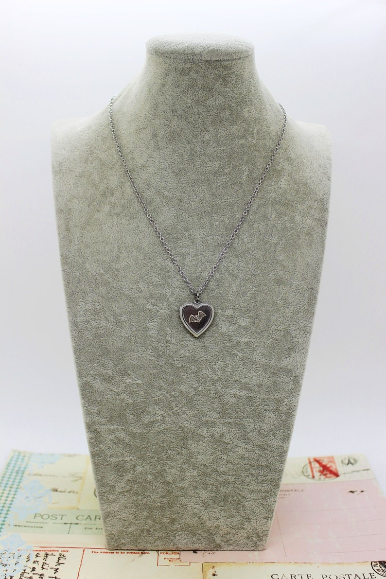 May include: A silver chain necklace with a heart-shaped pendant featuring a bat design.