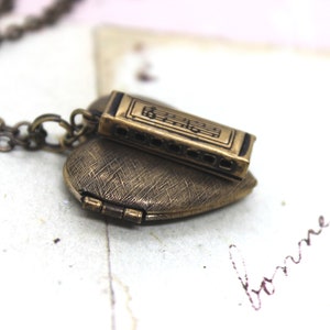 May include: A gold heart-shaped locket necklace with a small harmonica charm. The harmonica charm has musical notes engraved on it.