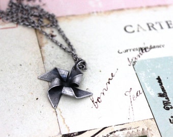 May include: A silver necklace with a silver pinwheel pendant. The pendant is a simple design with five points.