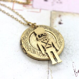 May include: Gold tone necklace with a locket pendant featuring a cutout silhouette of a toy soldier. The locket has a detailed floral design.