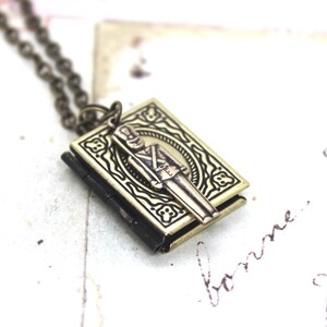 May include: A gold-toned necklace with a locket shaped like a book. The locket features an embossed design of a toy soldier.