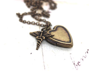Puede incluir: Un collar de oro con un dije en forma de corazón y un dije con un símbolo médico. El dije está abierto y la cadena es visible.