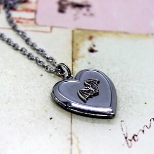 May include: A silver heart-shaped locket necklace with a small bat charm. The locket is open and the inside is blank.
