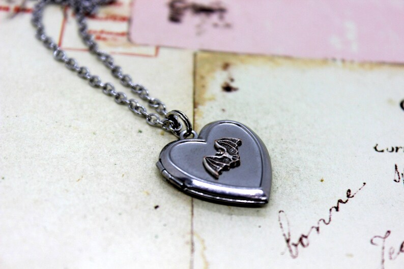May include: A silver heart-shaped locket necklace with a small bat charm. The locket is open and the inside is blank.