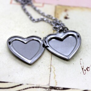 May include: A silver heart-shaped locket necklace with a chain. The locket is open, revealing the empty interior.