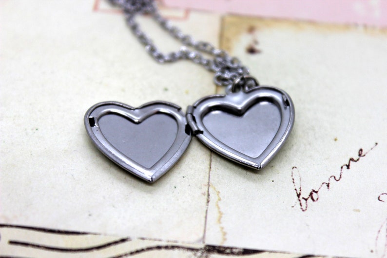 May include: A silver heart-shaped locket necklace with a chain. The locket is open, revealing the empty interior.