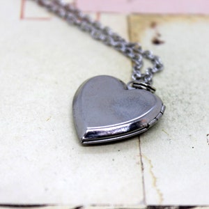 May include: A silver heart-shaped locket on a silver chain necklace. The locket is closed and has a smooth, shiny surface.