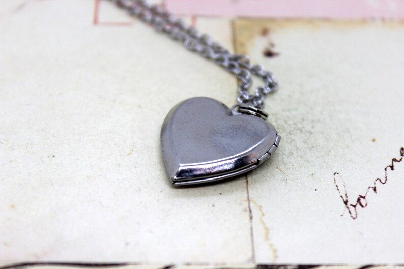 May include: A silver heart-shaped locket on a silver chain necklace. The locket is closed and has a smooth, shiny surface.