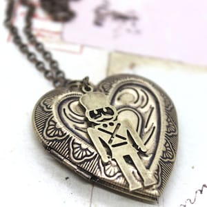 May include: A heart-shaped locket necklace with a bronze finish. The locket features an embossed design and a soldier figure. The necklace chain is also bronze. The locket is on a white surface.