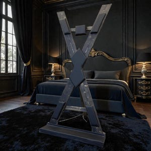 May include: A dark stained wooden cross-shaped structure with black padded supports. The structure is in a bedroom with a black rug, bed, and furniture. The room has dark walls and curtains.