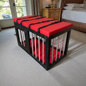 May include: A black and red pet crate with metal bars. The crate has a red padded top and bottom, secured with black straps. The frame is black, and the bars are silver.