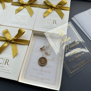 Crème doos uitnodigingsset; Heldere, goudkleurige acryluitnodiging met gepersonaliseerde zegelwas en droogbloemen met speciale dozen met linten