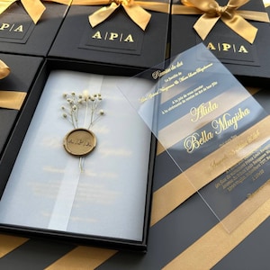 Schwarzes Einladungsset in einer Box; Einladung mit Golddruck aus klarem Acryl mit personalisiertem Siegelwachs und Trockenblumen sowie speziellen Boxen mit Bändern