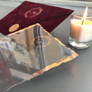 Puede incluir: Una invitación de boda de acrílico transparente con un borde de lámina dorada y una corona de lámina dorada con las iniciales "C & W" en el centro. El texto de la invitación dice "Vous êtes invités au mariage de Claire & William Le 2 avril 2022 Primordia."