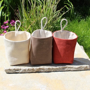 May include: Three fabric hanging storage baskets with rope handles. The baskets are beige, brown, and red. The baskets are lined with a white and brown striped fabric.