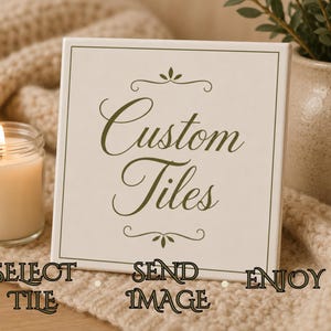 May include: A square, off-white tile with the words "Custom Tiles" in elegant script. The tile is framed in a thin, dark border and decorated with floral accents. A lit candle in a glass jar and a beige knitted blanket are in the background.