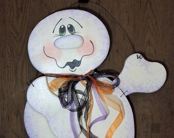 May include: A white ghost with a purple and white painted design. The ghost has a big, round, white nose and green eyes. The ghost is wearing a purple, orange, and black ribbon around its neck.