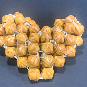 Puede incluir: Una guirnalda de cuentas de madera en forma de corazón con tonos marrones y beige naturales. Las cuentas están conectadas por un hilo blanco delgado.