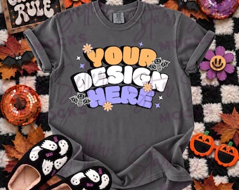 May include: A charcoal gray short-sleeve t-shirt featuring the text YOUR DESIGN HERE in orange, white, and purple bubble letters, accented with small flowers, stars, and two bat illustrations. The shirt is displayed with black ghost-patterned slippers.