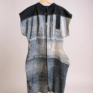 May include: A sleeveless denim dress with a black top section and a full-length zipper. The dress is made of various denim patches in shades of gray and blue, with a small pocket and a metal ring detail.