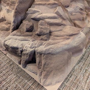 Può includere: Modello dettagliato e strutturato di una catena montuosa marrone chiaro. Il modello presenta picchi, scogliere e valli, con un aspetto ruvido e naturalistico. La base è di colore beige chiaro.