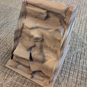 Può includere: Uno sfondo per terrario strutturato, color beige, con un design a strati di roccia. Il pezzo rettangolare ha una base piatta e una facciata rocciosa angolata, creando un aspetto naturalistico. La superficie ha una consistenza ruvida, simile alla pietra.