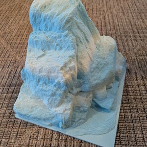 以下が含まれることがあります： 岩山を模した、テクスチャ加工が施された水色の模型。模型は等高線のある長方形の基盤を持っています。山は、青と白の様々な色合いを持つ、ざらざらとした不均一な表面をしています。