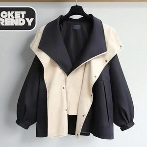 Peut inclure: Veste noire et crème avec un design unique. La veste présente un panneau avant et un col crème, avec un corps et des manches noirs. La veste a une fermeture éclair et des boutons. Le texte "JACKET TRENDY" est dans un encadré noir.