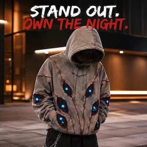 Op de afbeelding: Een grijze hoodie met meerdere donkere, amandelvormige oogafbeeldingen met lichtgevende blauwe centra en rode gestikte randen. De tekst STAND OUT. OWN THE NIGHT. staat in wit en rood gedrukt boven de hoodie.