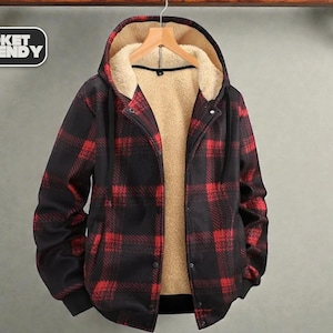 May include: A black and red plaid jacket with a hood and a warm, beige interior. The jacket has a button-up front and a black ribbed hem. The text "JACKET TRENDY" is in a white box in the upper left corner.