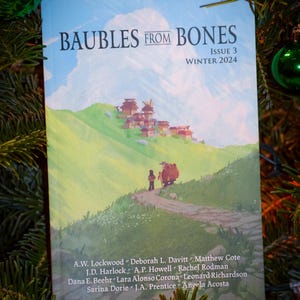 May include: A magazine cover with a blue sky and white clouds. The title is "Baubles From Bones" with the subtitle "Issue 3 Winter 2024". The cover features a colorful illustration of a person walking on a path in a mountainous landscape.