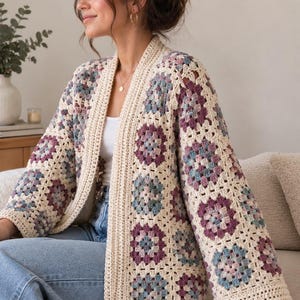 May include: A crochet cardigan featuring a granny square pattern in shades of cream, dusty rose, and muted blue. The garment has an open front, long sleeves, and a solid cream-colored ribbed border along the neckline, front opening, and sleeve cuffs.