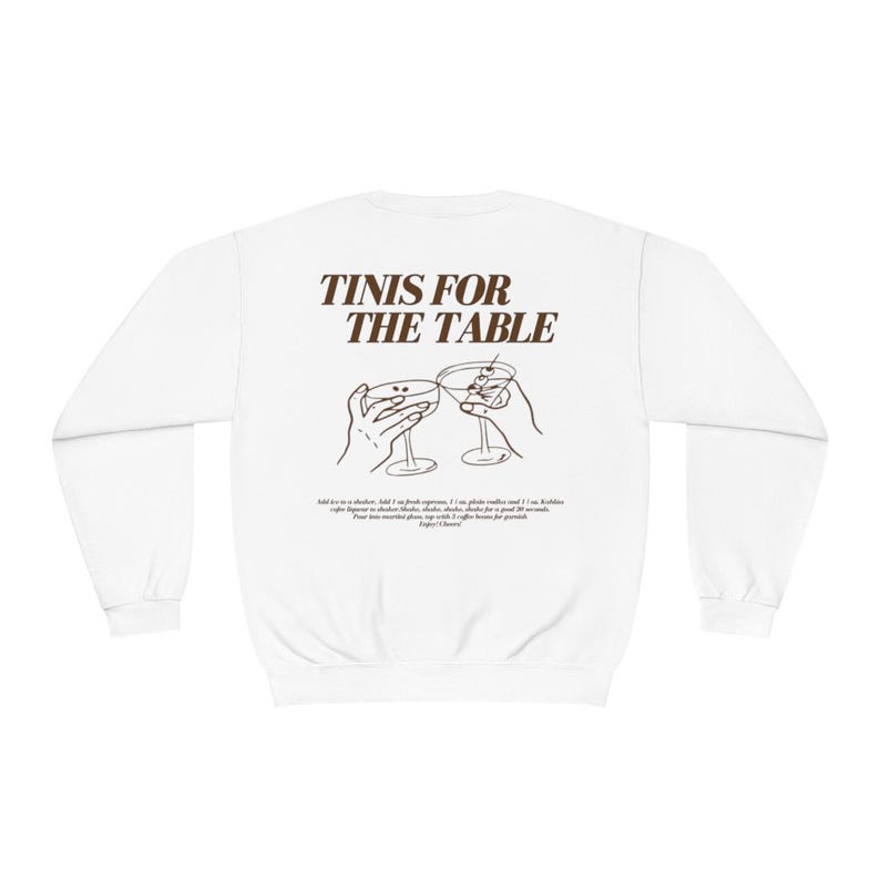 May include: White sweatshirt with brown text that reads "TINIS FOR THE TABLE" and a line drawing of two hands holding up martini glasses.