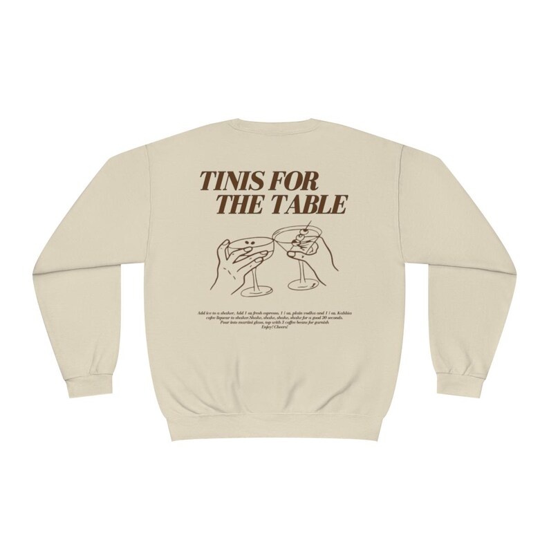May include: A beige sweatshirt with the text "TINIS FOR THE TABLE" printed in brown on the back. The text is surrounded by a graphic of two hands holding up martini glasses.