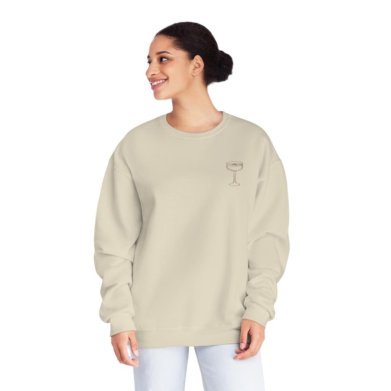May include: A light beige sweatshirt with a small embroidered image of a champagne flute on the left chest.