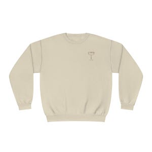 May include: A beige sweatshirt with a simple line drawing of a wine glass on the front.