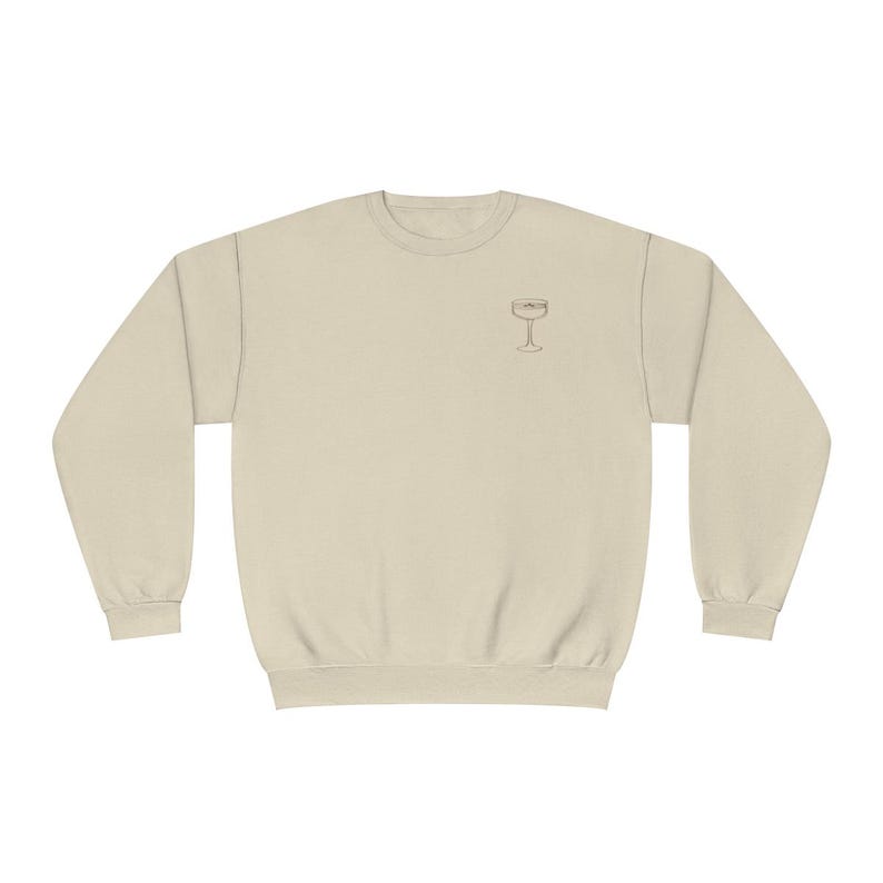 May include: A beige sweatshirt with a simple line drawing of a wine glass on the front.