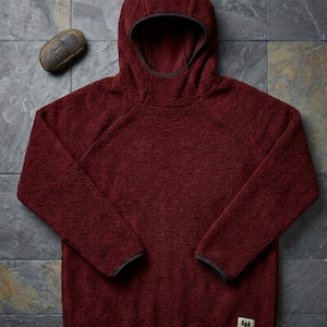 May include: A deep burgundy long-sleeve hooded sweatshirt made of a textured, fuzzy fleece material. The pullover features a hood with dark trim, raglan sleeves, and a small rectangular patch on the lower front corner with a tree graphic and text.