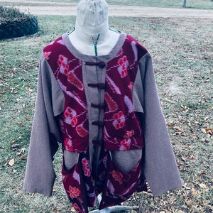 May include: A brown and grey jacket with a red and pink patterned front. The jacket has a mandarin collar and a button closure. The jacket is on a white mannequin.