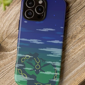 May include: A blue and green phone case featuring a pixelated design of a creature with a yellow outline against a night sky with clouds and stars. The case is on a wooden surface.